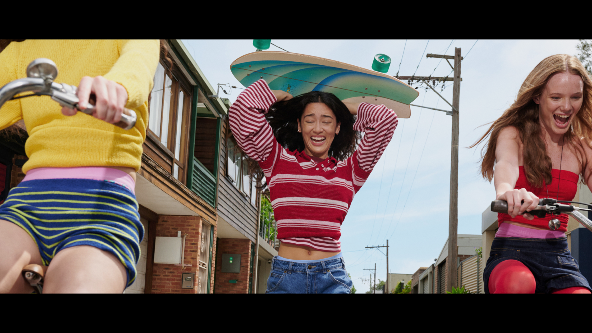 שלוש נערות שמחות רצות ורוכבות על אופניים ברחוב – תמונה הממחישה את חופש התנועה, שמחת החיים והאנרגיה שמתאפשרת כאשר משתחררים מעול כלכלי (כמו 'המס הוורוד') ומגבלות פיזיות