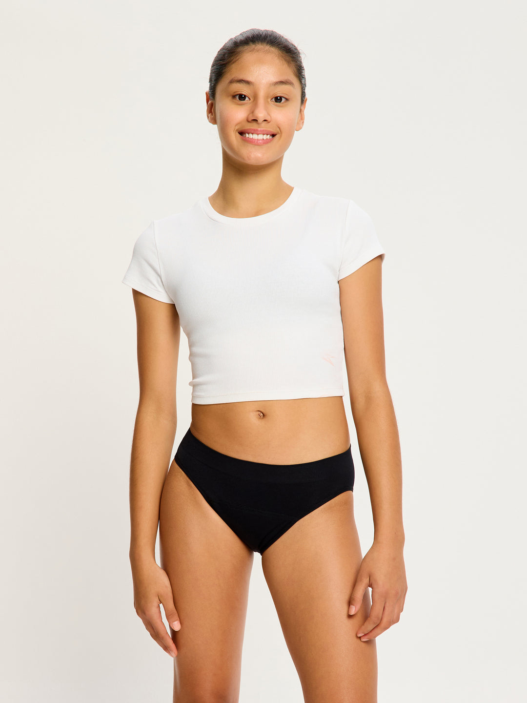 נערה לובשת תחתון סופטסטרצ' ביקיני בצבע שחור, מבט מהחזית, מדגיש את הגזרה ללא תפרים וכיסוי הישבן המלא. מידת הדוגמנית- Youth Small